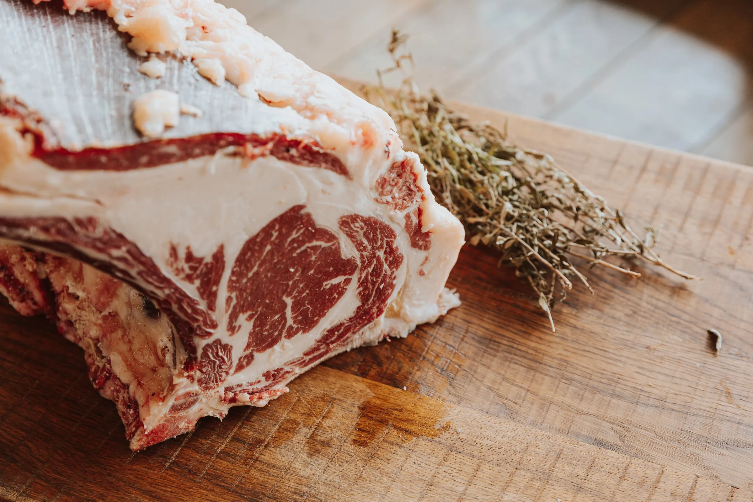 De snede van een rauw ribstuk op een houten plank: rood vlees met fijne witte vetadertjes onder een dikke vetrand