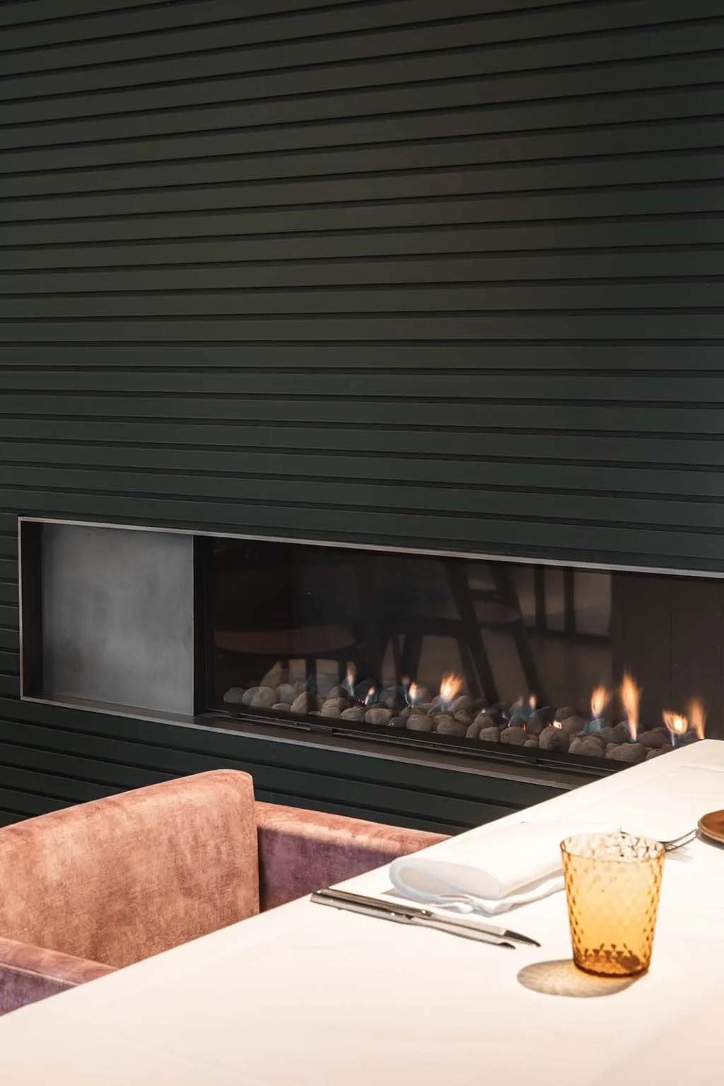 De gashaard in de donkergroene lattenwand, met een gedekte tafel en een amberkleurig glas ervoor