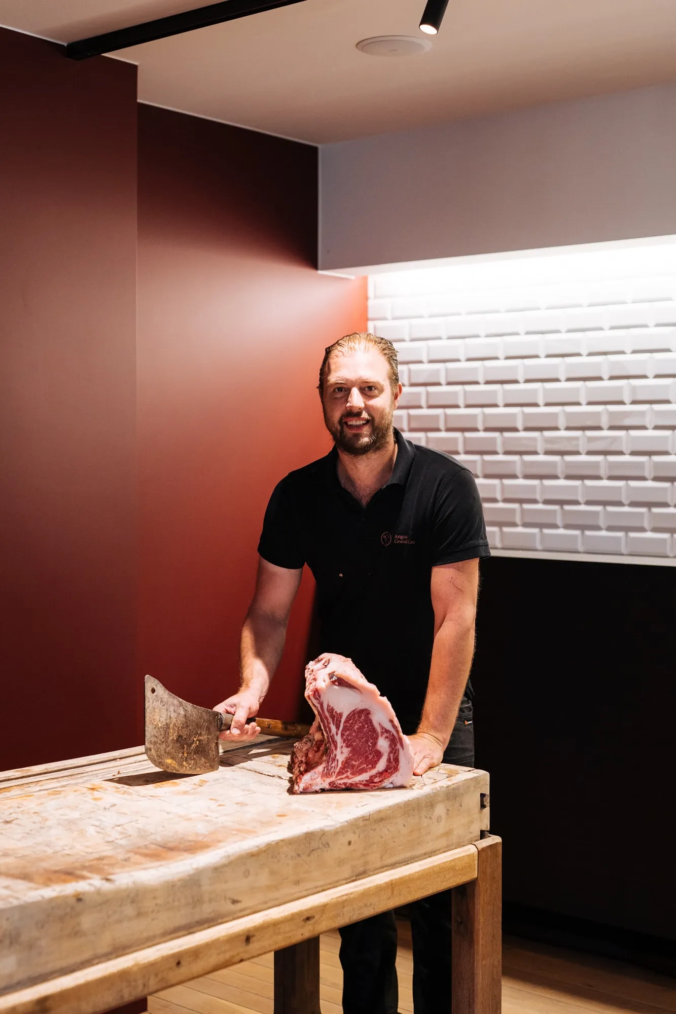 Ludovic Ghyselen in een zwarte polo aan het kapblok, met een hakmes en een stuk rundvlees met been