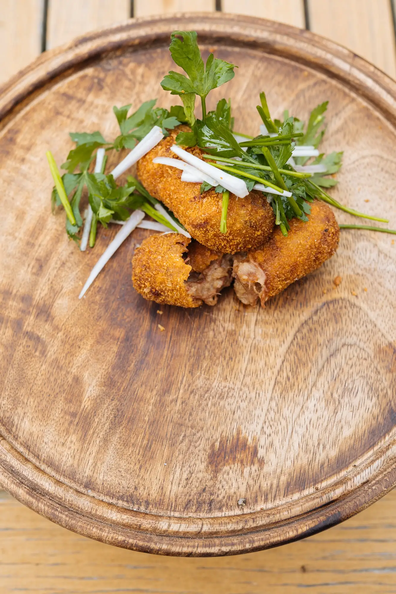 Drie goudbruine kroketten met een toef kruidensla op een houten bord